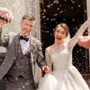 Happy bride and groom celebrating outside chapel, showered with confetti, joyful wedding moment captured perfectly.