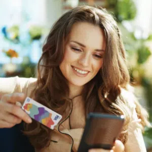 Woman smiles while shopping online with smartphone and colorful credit card.