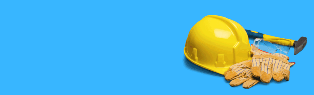 Yellow hard hat, work gloves, safety goggles, and hammer on blue background, symbolizing construction safety gear.