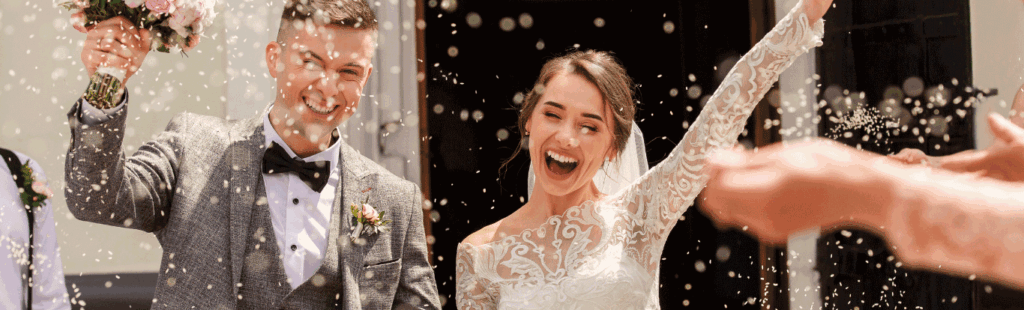 Happy bride and groom celebrate with confetti outside venue, capturing the joy of their wedding day moment.
