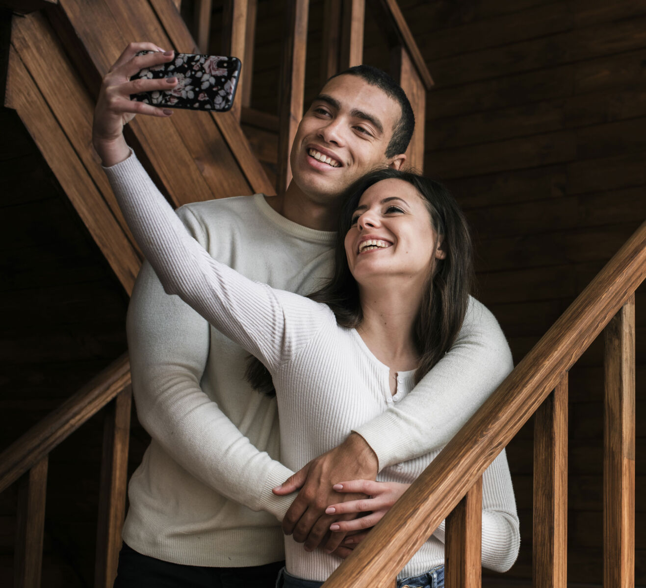 A happy couple taking a selfie together on a wooden staircase, smiling and embracing affectionately.