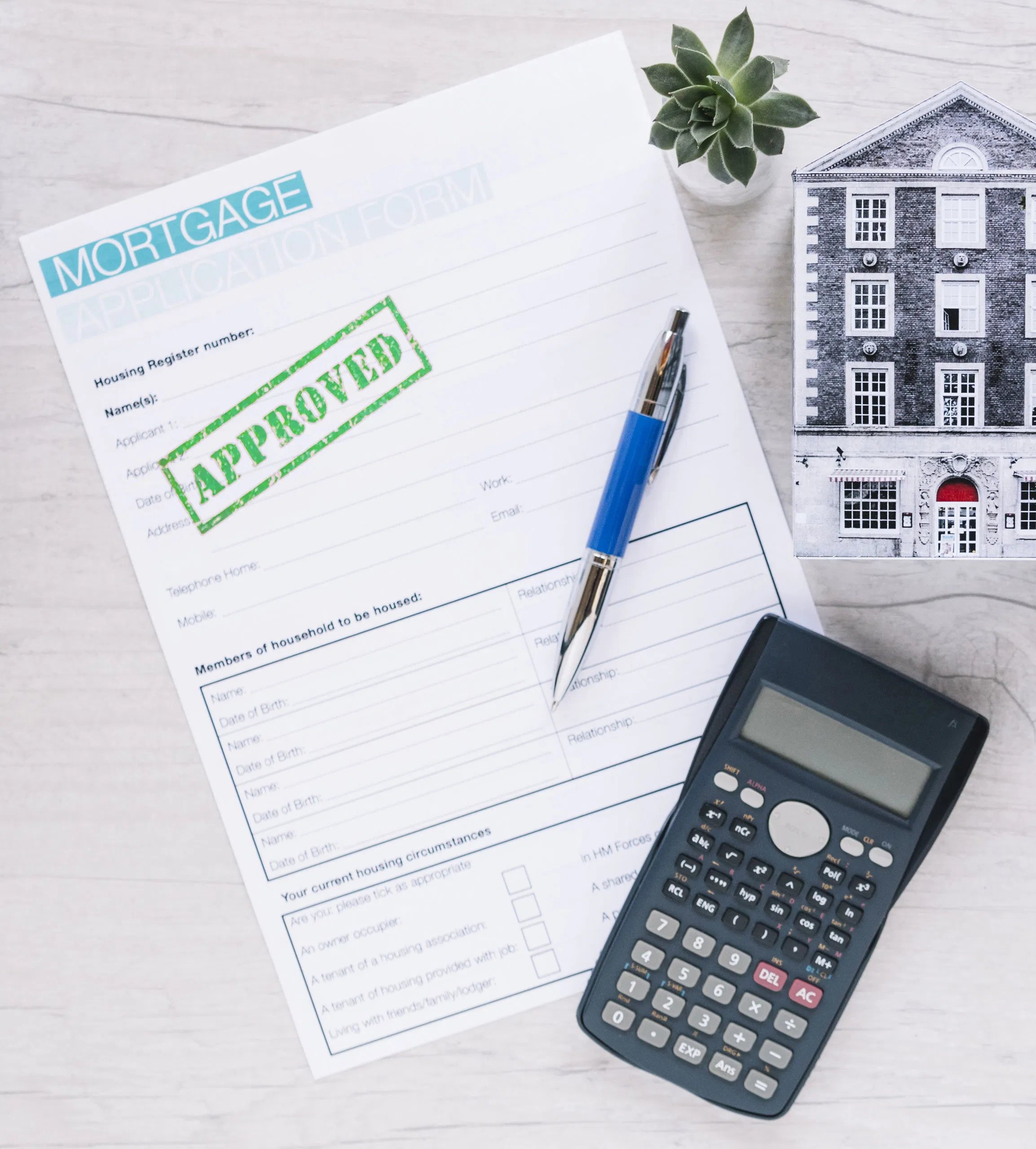 Mortgage approval form with green Approved stamp, calculator, pen, house model, and plant on table.