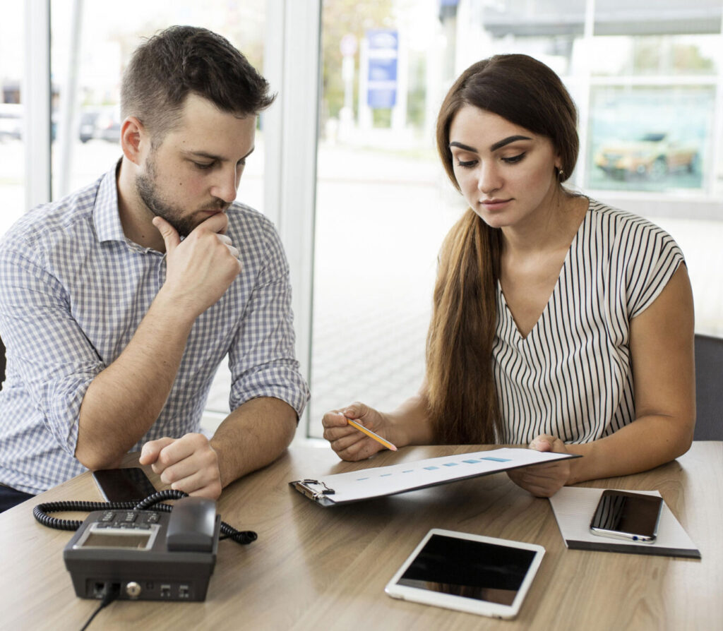 Business meeting with two professionals reviewing a document and graphs on a clipboard in a modern office.