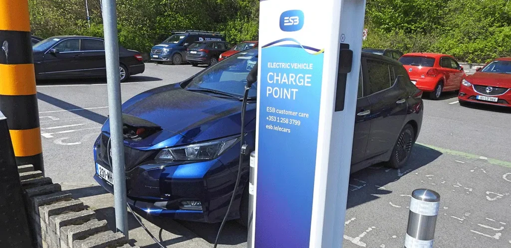 Electric car charging at ESB charge point in parking lot under sunny skies.