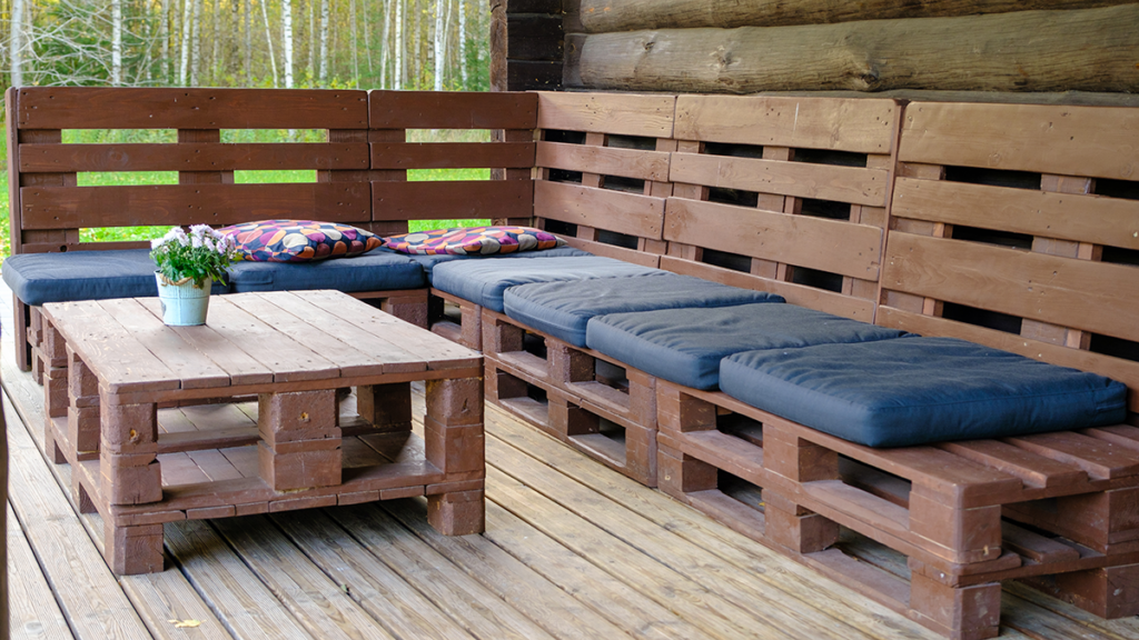 Rustic outdoor patio furniture made from wooden pallets with cushioned seating and a potted plant on the table.
