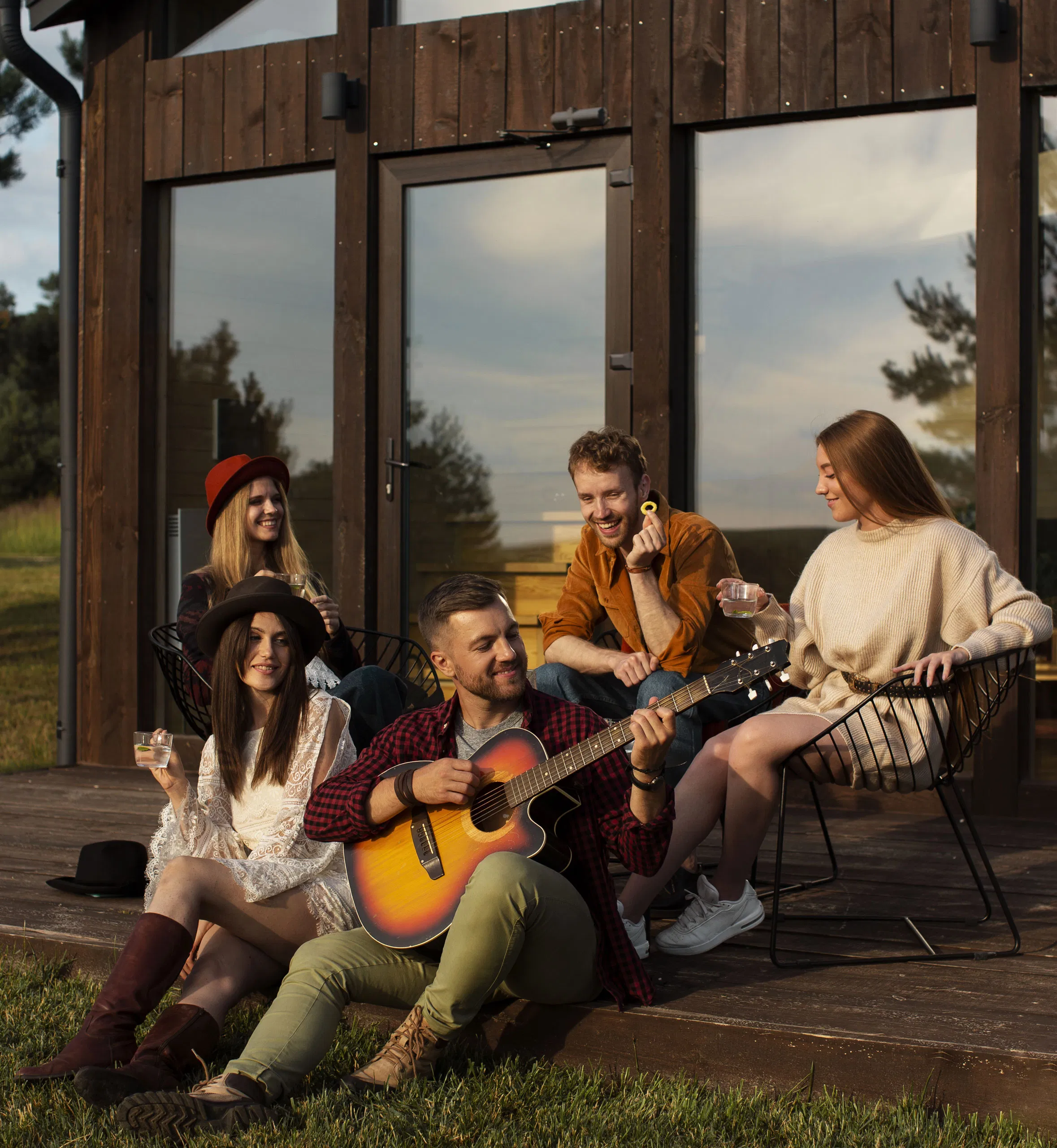 Group of friends enjoying music and drinks on a sunlit cabin porch, highlighting outdoor leisure and camaraderie.