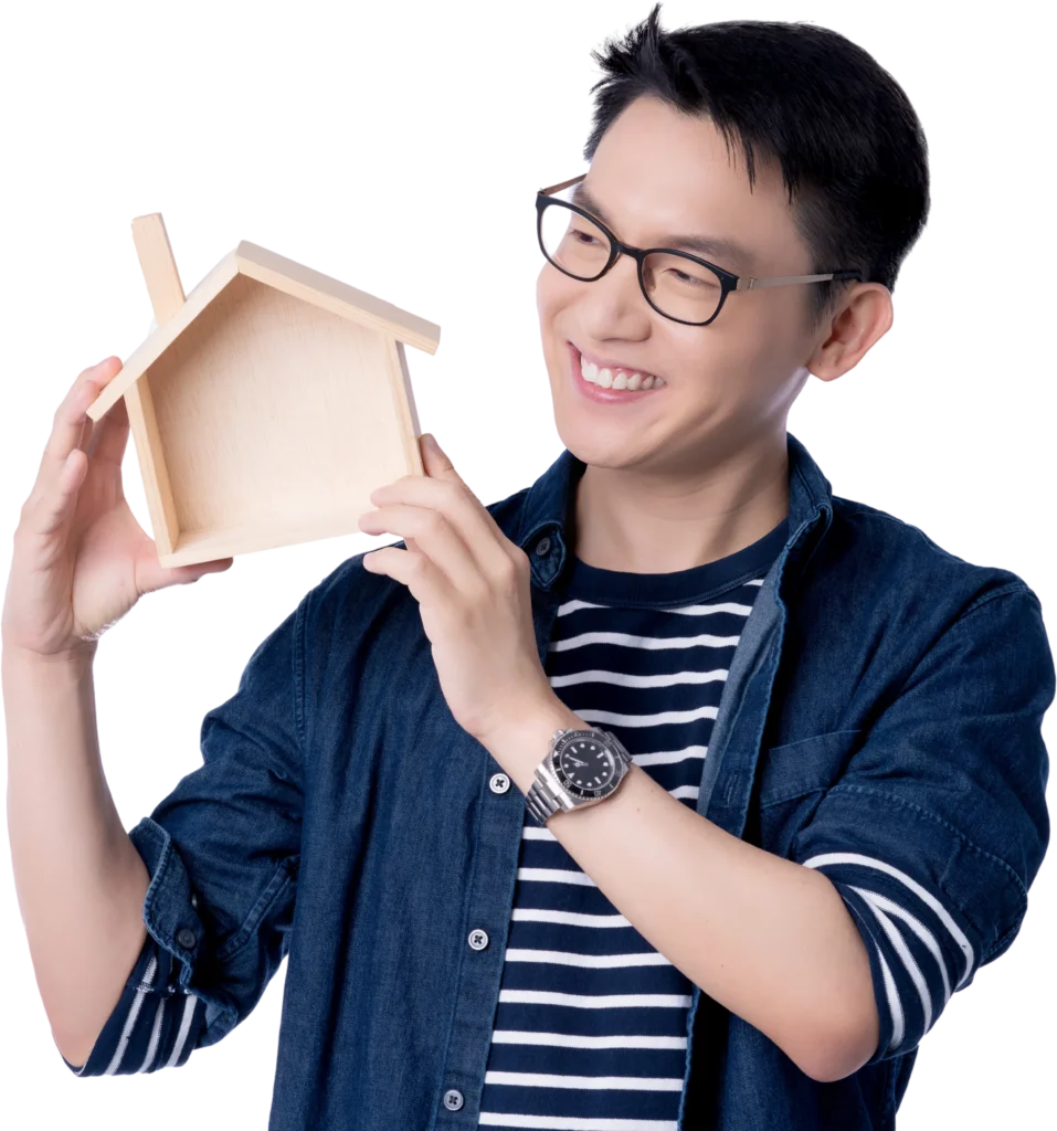 Man smiling, holding a small wooden house model, wearing glasses and striped shirt, denim jacket.