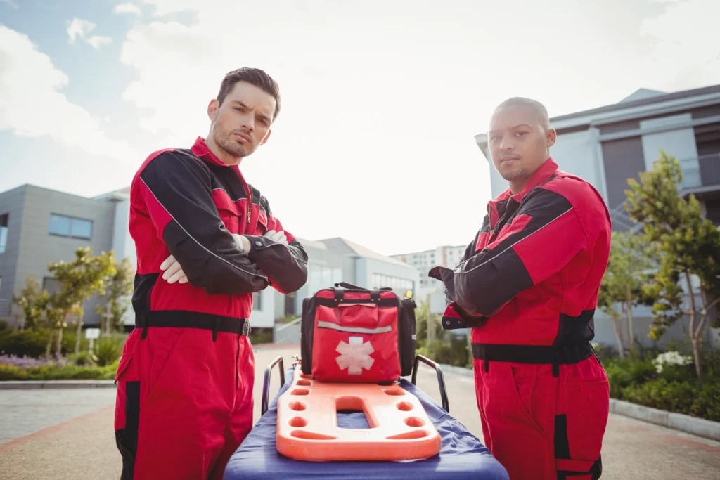 Paramedics stand confidently by a stretcher, ready for emergency response in red uniforms.