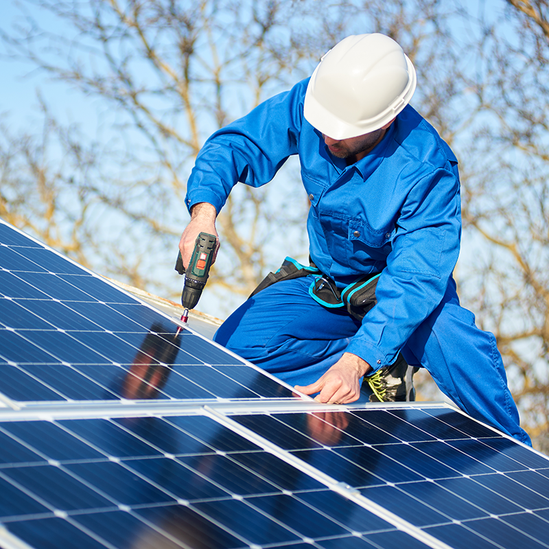 Technician in blue uniform and helmet installing solar panels outdoors.