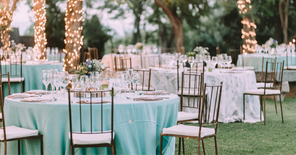 Elegant outdoor wedding reception with tables set, twinkling lights, and chairs on a grassy landscape.