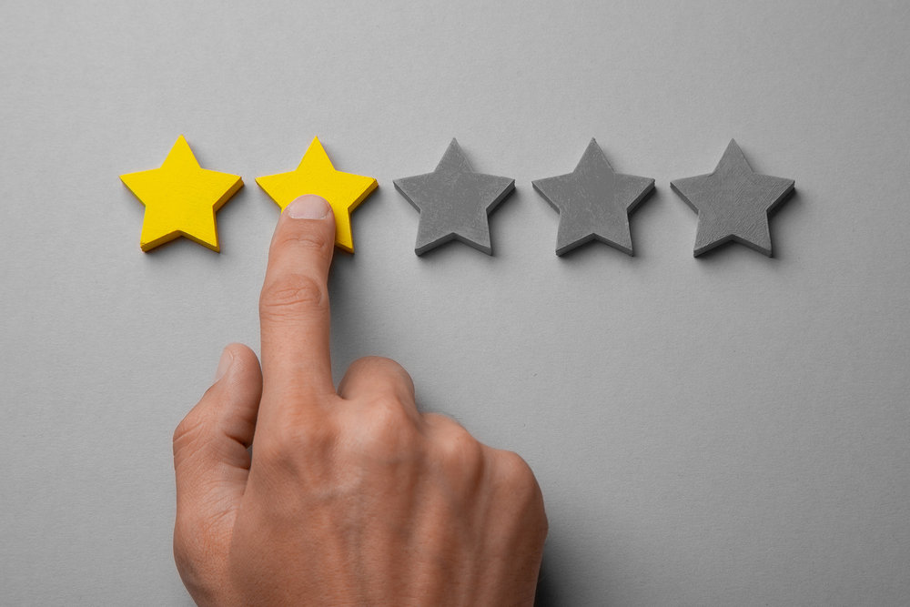 Hand pointing at a two-star rating on gray background, symbolizing low customer satisfaction or feedback.