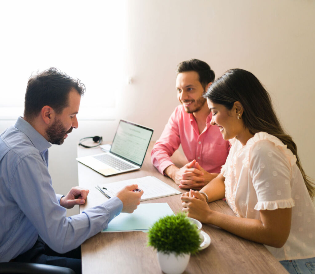 Man consulting couple in office setting with laptop and documents, highlighting communication and partnership.