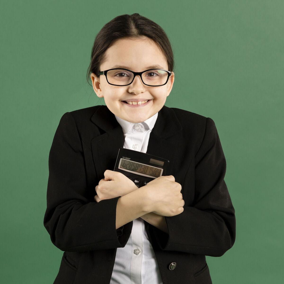 Young girl in black suit holding calculator, smiling against green background.