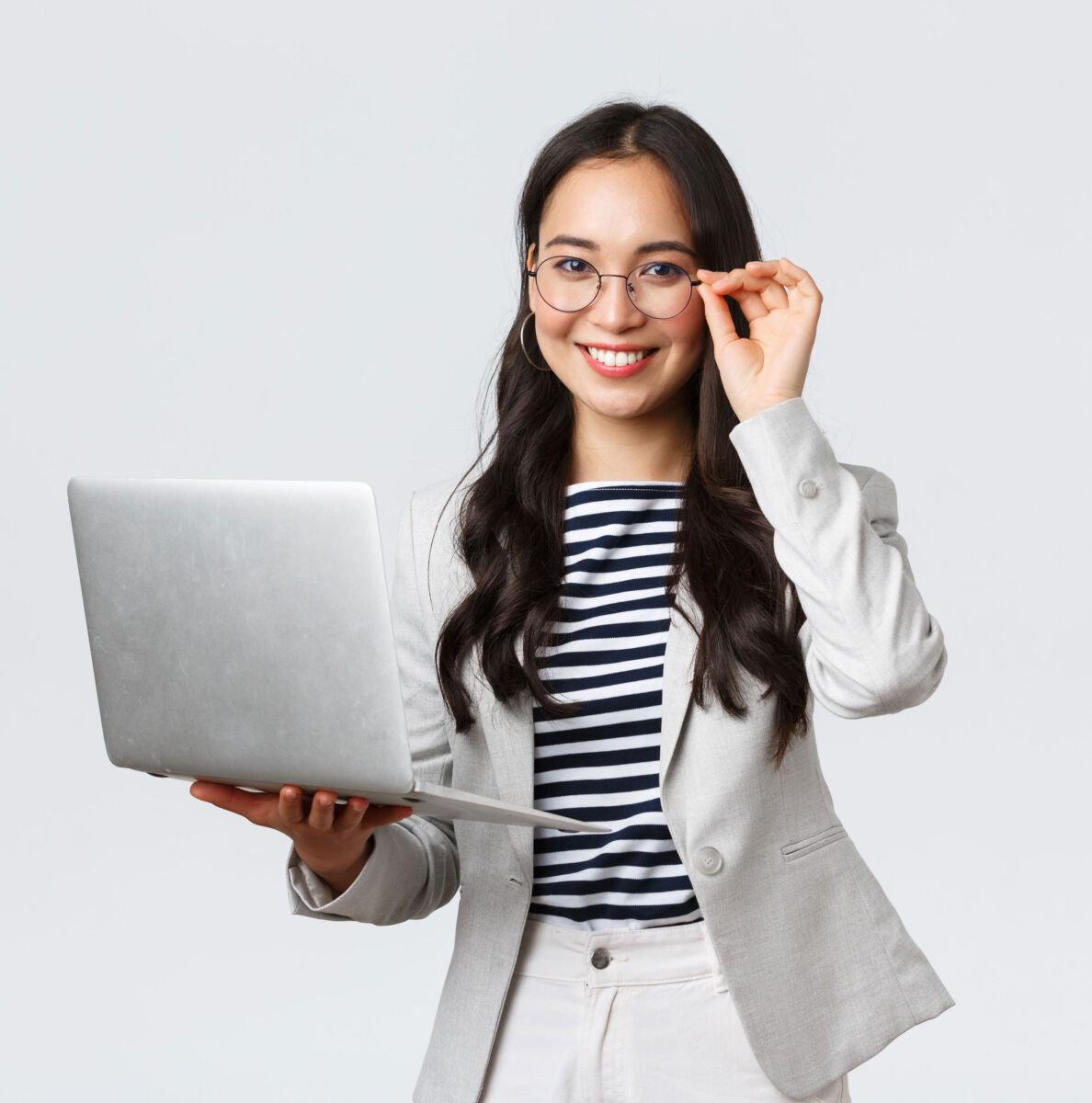 Professional woman smiling with laptop, wearing glasses and a striped shirt, isolated on white background.