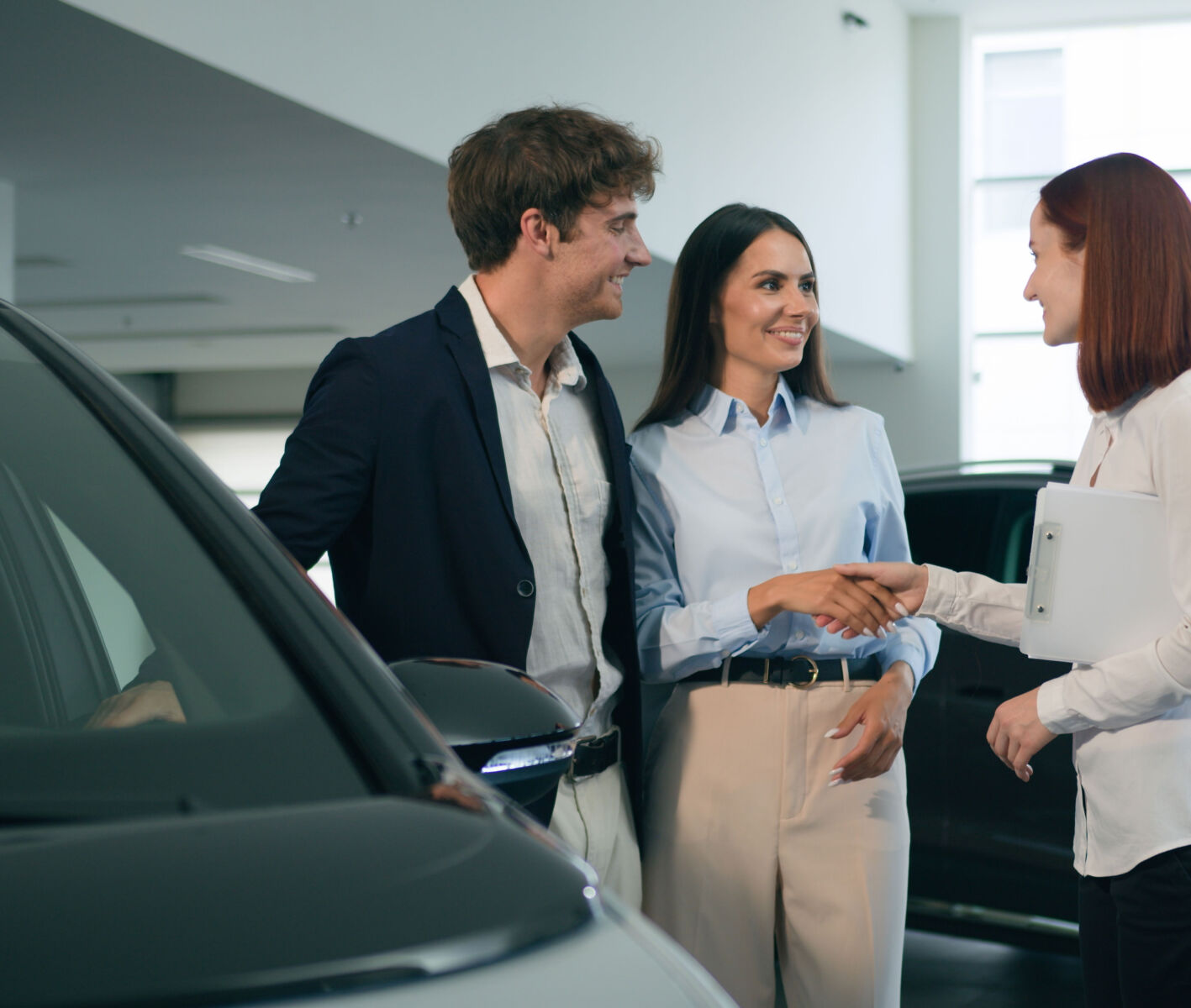 Couple shaking hands with car dealer in showroom, purchasing new vehicle.