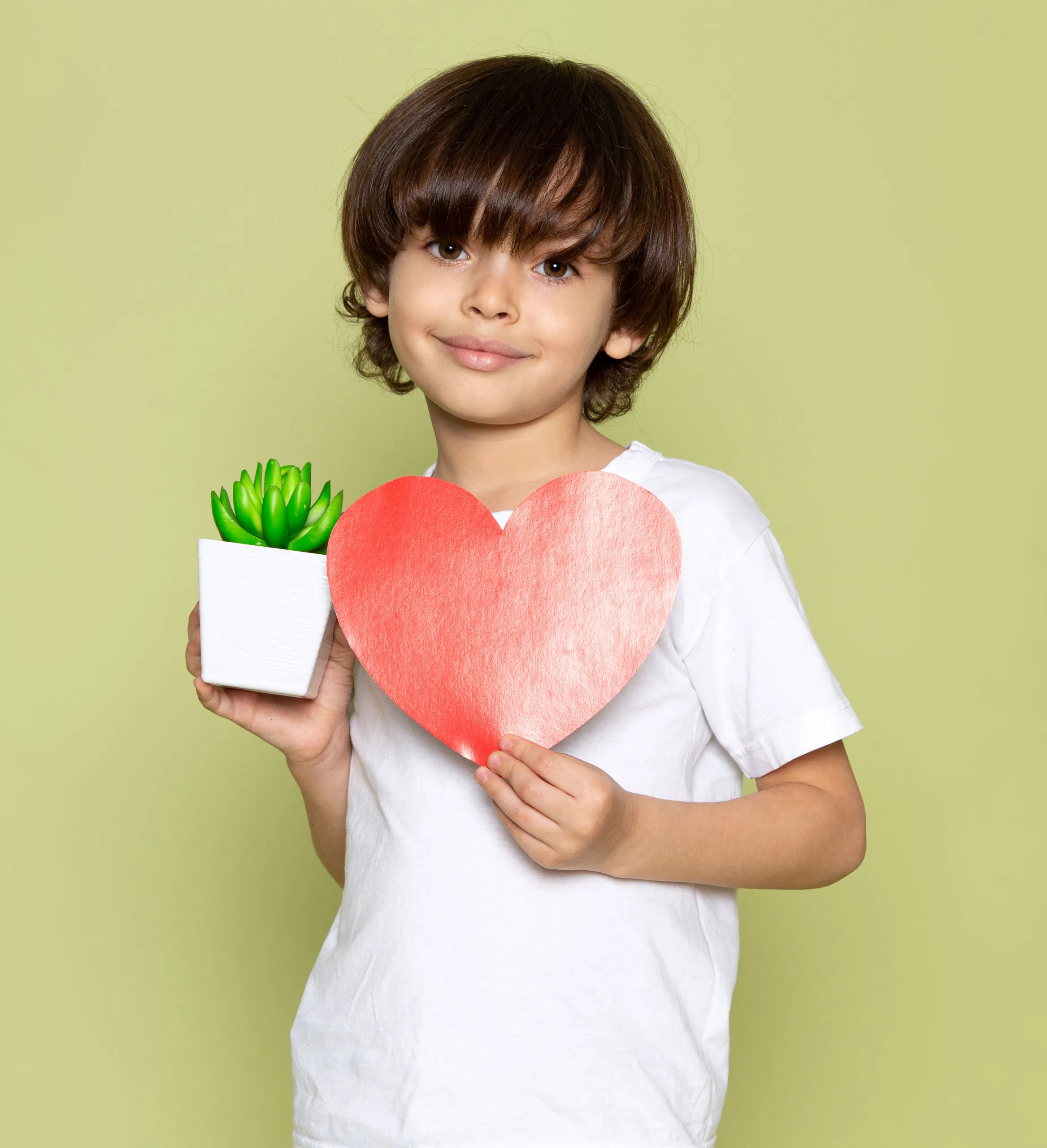 Child holding a red heart and a potted succulent against a light green background.