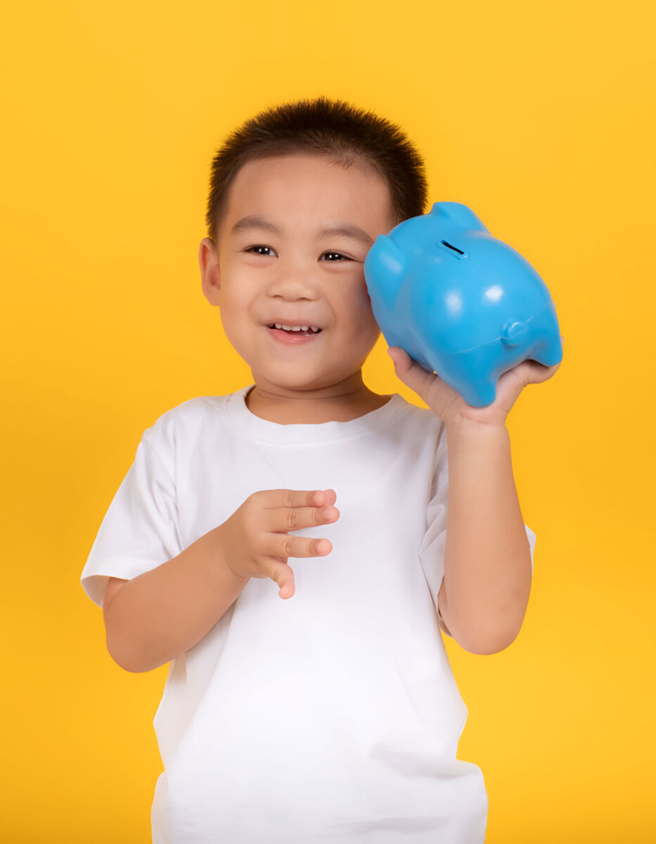 Child smiling while holding a blue piggy bank against a bright yellow background.