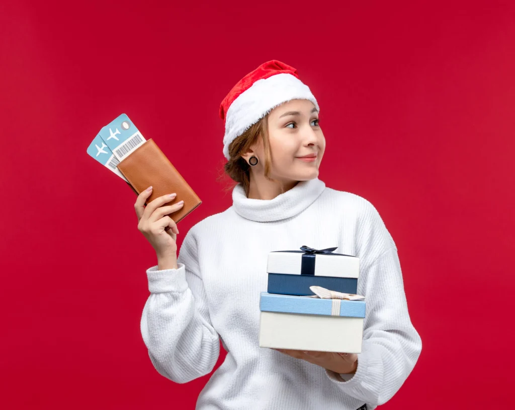 Woman in Santa hat with travel tickets and gift boxes, festive red background.