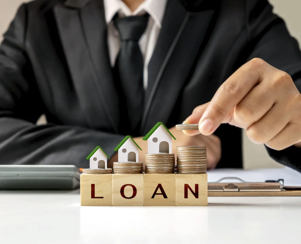 Businessman stacking coins on blocks spelling loan, symbolizing home loan investment.