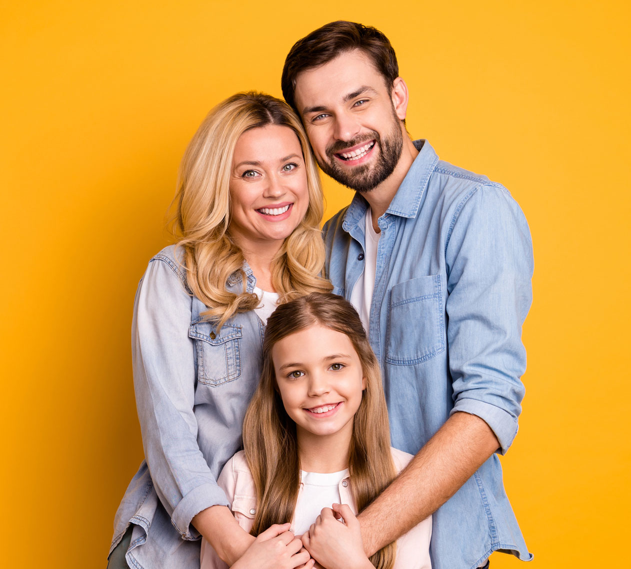 Happy family of three smiling in front of a bright yellow background, wearing casual denim outfits.