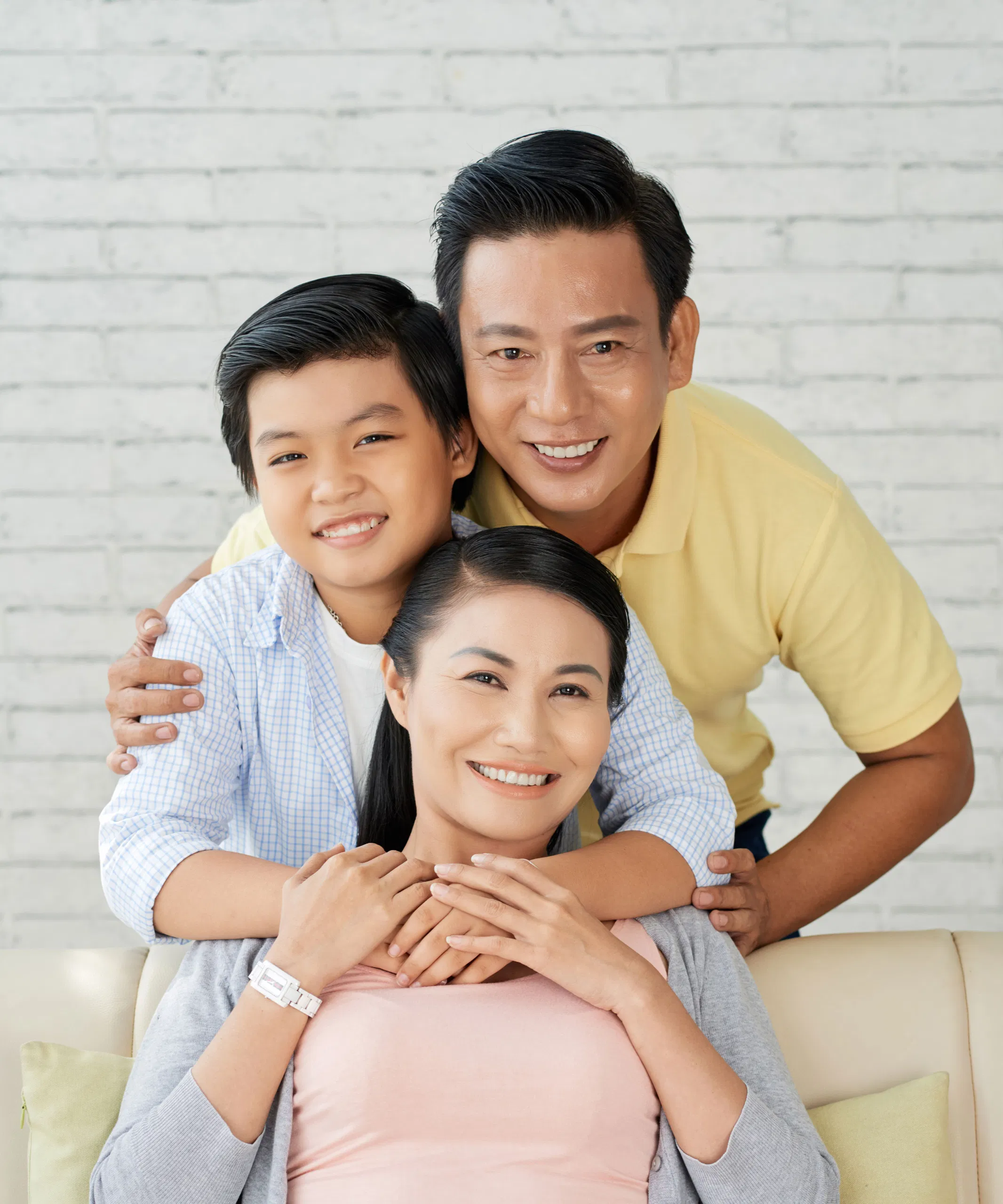 Smiling family posing together on sofa against a light brick wall background.