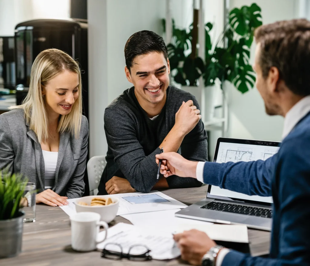 Happy business meeting with a couple discussing plans, with documents and laptop on office table.
