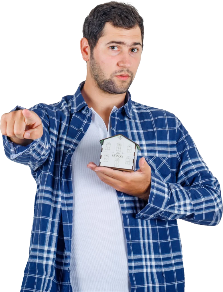 Man in blue plaid shirt holding house model, pointing forward, isolated on white background. Real estate concept.
