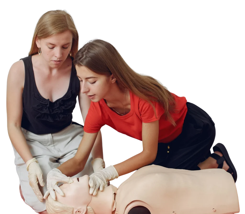 Two women practice CPR on a mannequin, focusing on rescue breathing technique while wearing disposable gloves.