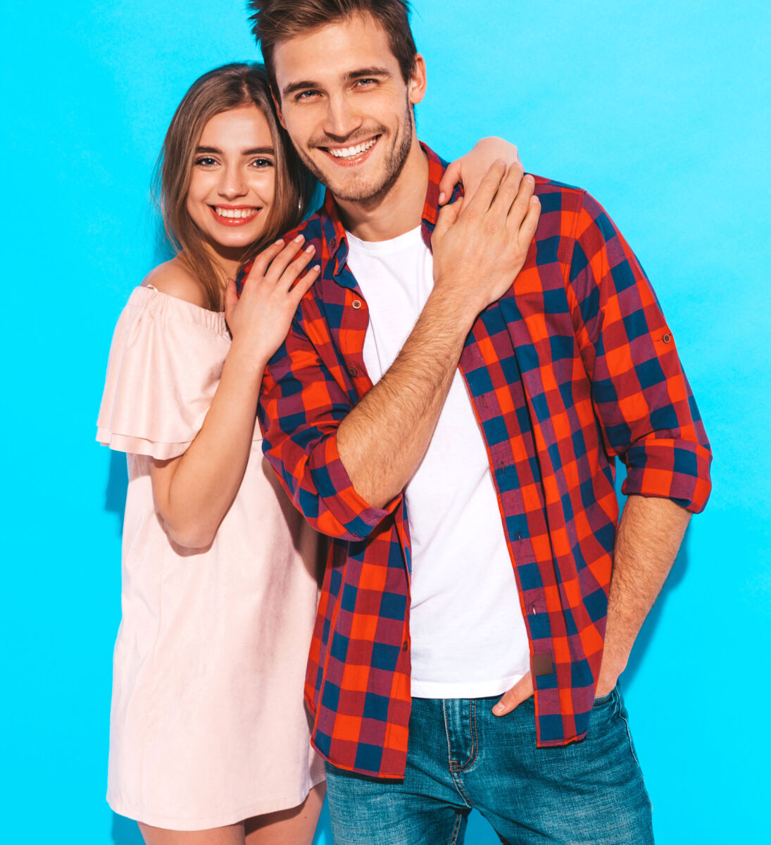 Smiling couple in casual attire against a blue background, embracing warmly.