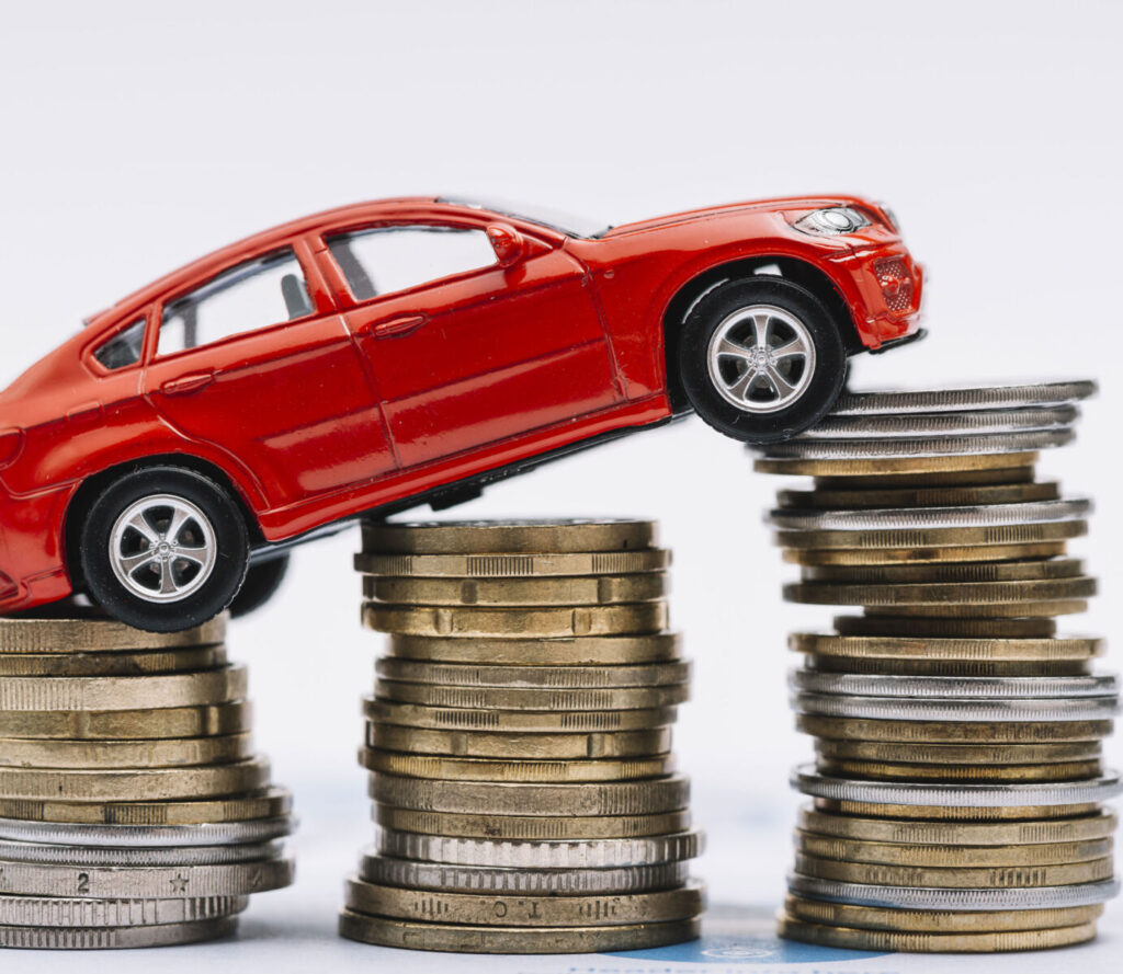 Red toy car climbing stacks of coins, symbolizing car financing or budgeting.